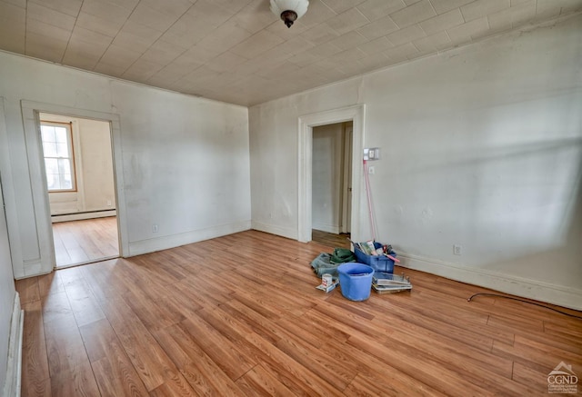 empty room featuring baseboard heating, crown molding, and light wood-type flooring