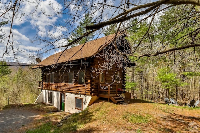 exterior space featuring a wooden deck, a shingled roof, and log exterior