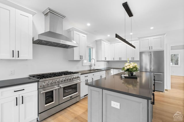 kitchen with a kitchen island, appliances with stainless steel finishes, sink, hanging light fixtures, and wall chimney range hood