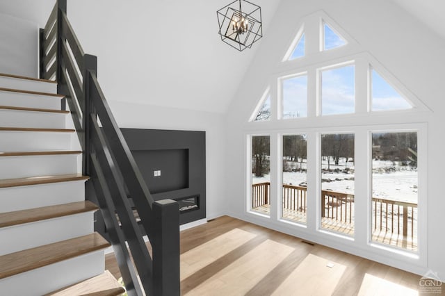 stairway featuring hardwood / wood-style flooring, an inviting chandelier, and high vaulted ceiling