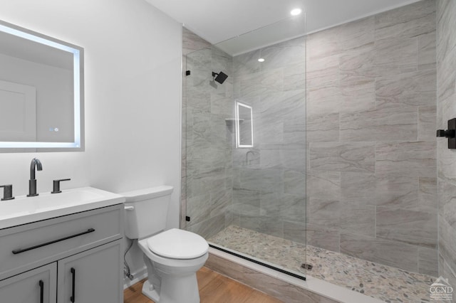 bathroom with vanity, wood-type flooring, a tile shower, and toilet