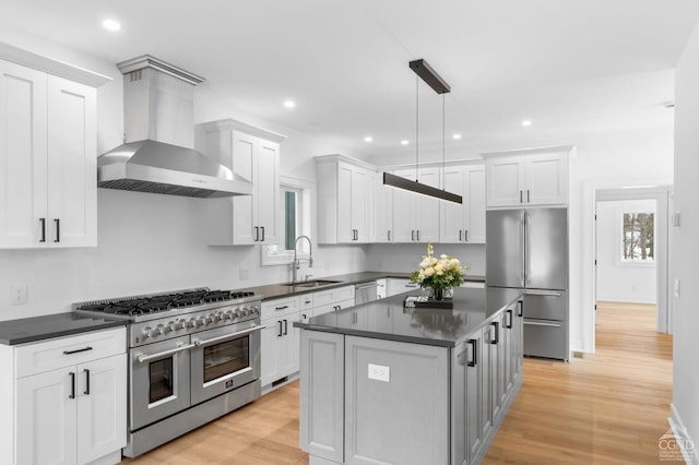 kitchen featuring wall chimney range hood, sink, stainless steel appliances, a kitchen island, and decorative light fixtures