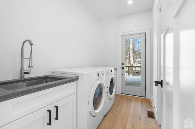 clothes washing area with separate washer and dryer, sink, cabinets, and light wood-type flooring