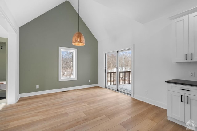 unfurnished dining area with high vaulted ceiling and light hardwood / wood-style floors