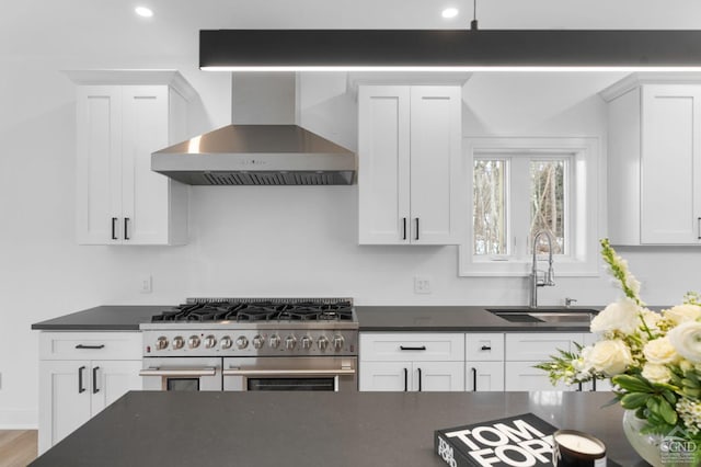 kitchen with white cabinets, sink, range with two ovens, and wall chimney range hood