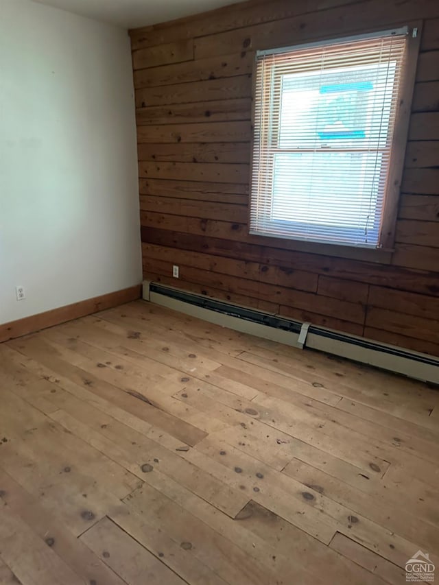 spare room with light hardwood / wood-style flooring, baseboard heating, and wooden walls