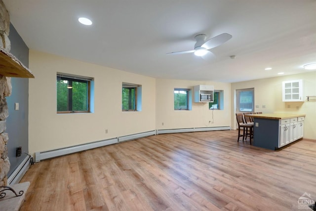 unfurnished living room with a wealth of natural light, ceiling fan, light hardwood / wood-style floors, and a baseboard heating unit