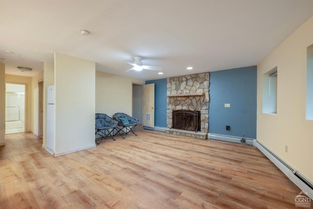 unfurnished living room with ceiling fan, a stone fireplace, light hardwood / wood-style flooring, and a baseboard radiator