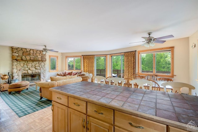 kitchen featuring tile countertops, a stone fireplace, light parquet flooring, and a healthy amount of sunlight