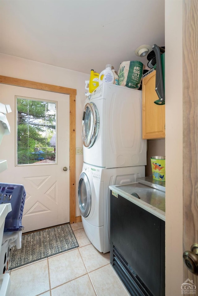 laundry area featuring cabinets, light tile patterned floors, and stacked washing maching and dryer