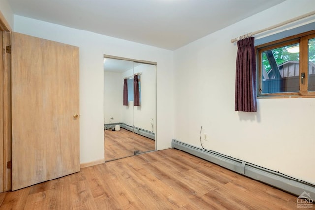 unfurnished bedroom with light wood-type flooring, a closet, and a baseboard heating unit