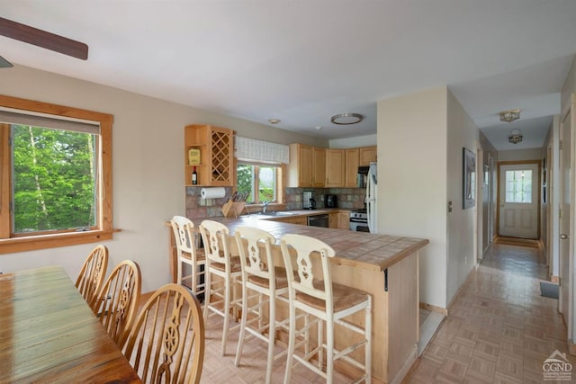 kitchen with tile counters, sink, backsplash, kitchen peninsula, and a kitchen bar