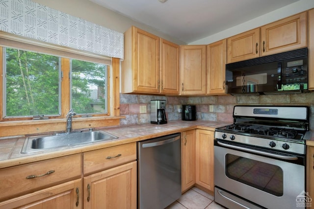 kitchen with backsplash, stainless steel appliances, sink, tile counters, and light tile patterned flooring