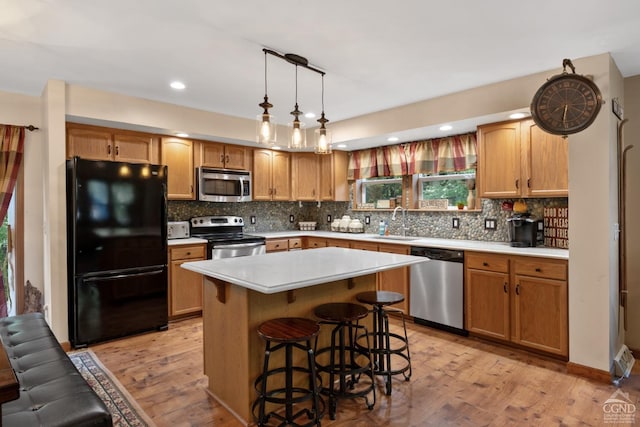 kitchen featuring sink, tasteful backsplash, appliances with stainless steel finishes, a kitchen island, and light wood-type flooring