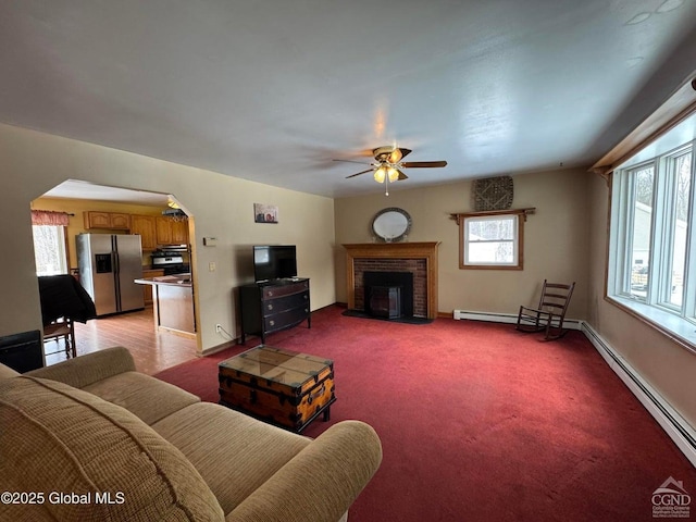 living area featuring baseboards, arched walkways, light carpet, and a fireplace