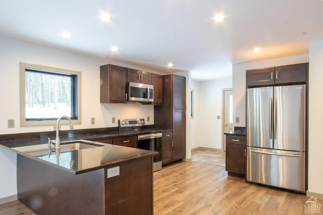 kitchen with dark brown cabinets, light wood-style flooring, a peninsula, stainless steel appliances, and a sink