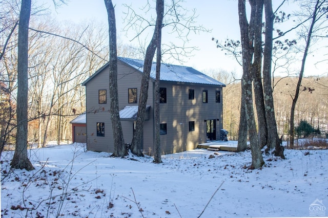 snow covered rear of property featuring metal roof and a garage