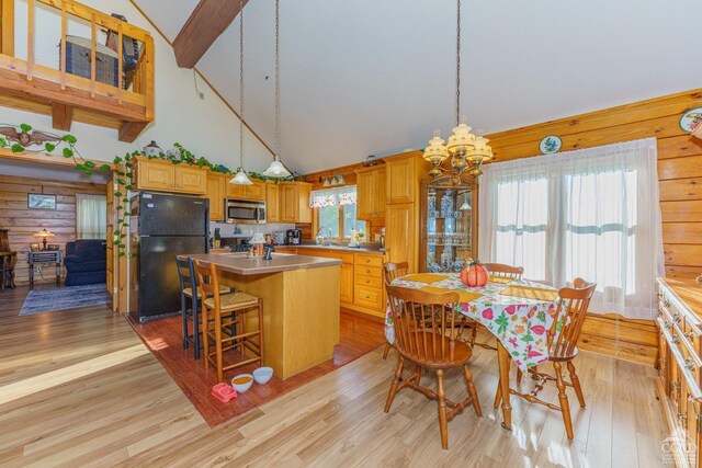 living room with a wood stove, high vaulted ceiling, wooden walls, light wood-type flooring, and beam ceiling