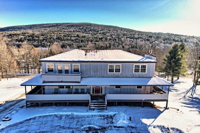 snow covered rear of property featuring a sunroom and a mountain view