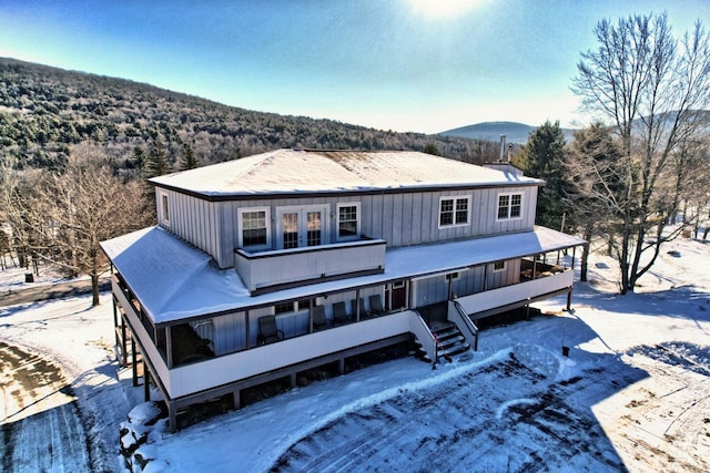 snow covered back of property featuring board and batten siding and a mountain view