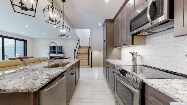 kitchen with appliances with stainless steel finishes, backsplash, light stone counters, sink, and hanging light fixtures