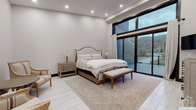 bedroom with access to exterior, light hardwood / wood-style flooring, and a towering ceiling