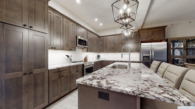 kitchen with light stone countertops, sink, a spacious island, decorative light fixtures, and appliances with stainless steel finishes