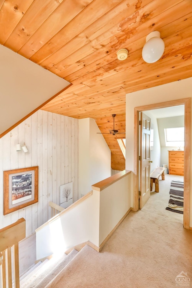 hall with wood walls, wooden ceiling, light carpet, and lofted ceiling with skylight