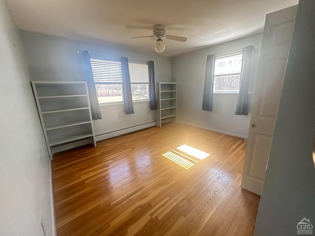 empty room featuring a wealth of natural light, a baseboard radiator, ceiling fan, and hardwood / wood-style floors