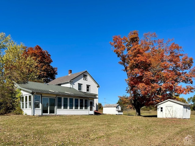 rear view of property with a lawn, a sunroom, and a storage shed