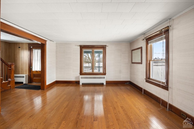 empty room featuring wood-type flooring, radiator, and wood walls