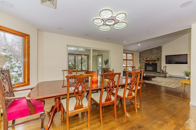 dining space with a stone fireplace, lofted ceiling, wood-type flooring, and baseboard heating