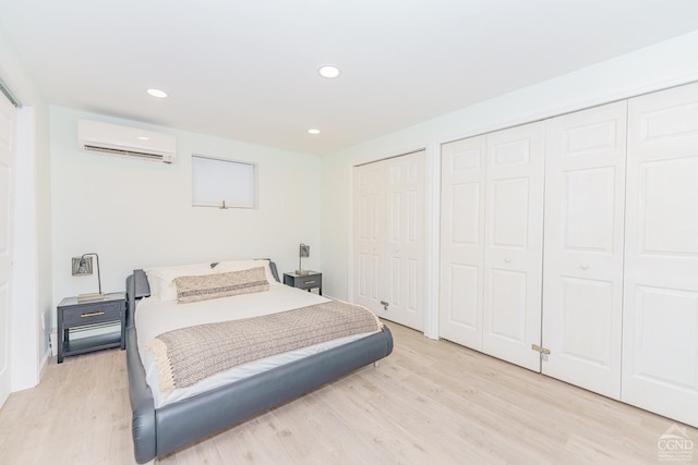 bedroom with a wall mounted air conditioner, two closets, and light hardwood / wood-style flooring