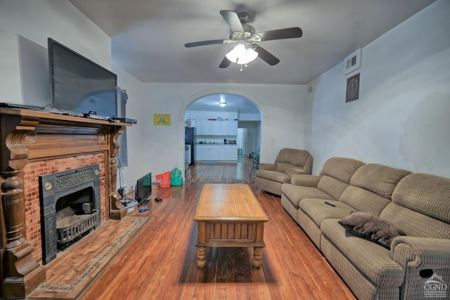 living room with a brick fireplace, ceiling fan, and hardwood / wood-style flooring