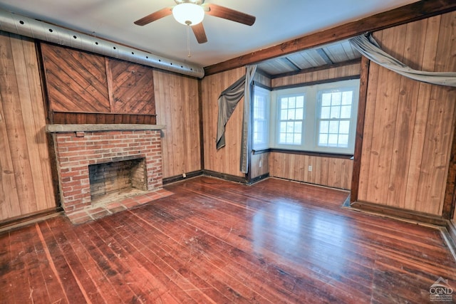 unfurnished living room featuring wooden walls, a brick fireplace, dark hardwood / wood-style floors, ceiling fan, and beamed ceiling