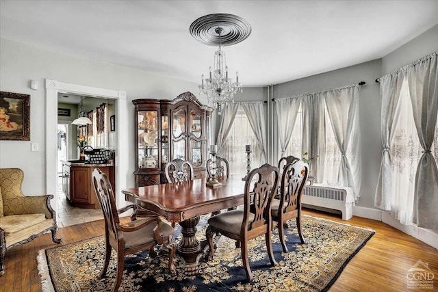 dining space with visible vents, baseboards, light wood-type flooring, radiator heating unit, and a notable chandelier