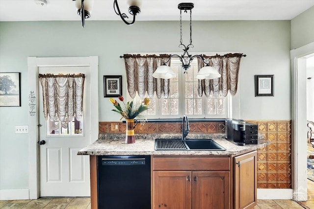 kitchen with light stone counters, brown cabinetry, stone finish floor, dishwasher, and a sink