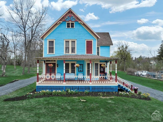 victorian-style house featuring covered porch, a front yard, and roof with shingles