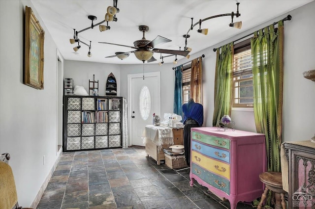 entryway with ceiling fan, a wealth of natural light, stone tile flooring, and baseboards