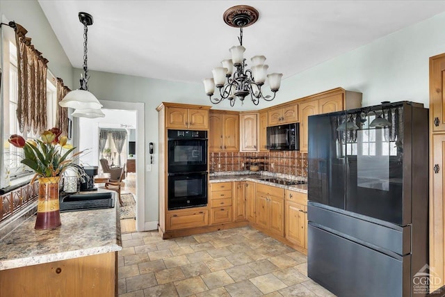 kitchen with an inviting chandelier, tasteful backsplash, black appliances, stone finish floor, and hanging light fixtures