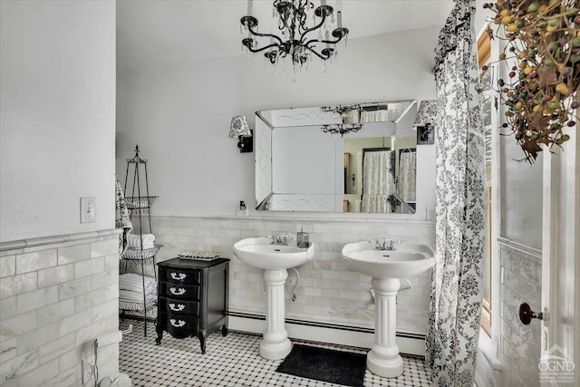 bathroom with a chandelier, wainscoting, tile walls, baseboard heating, and a sink