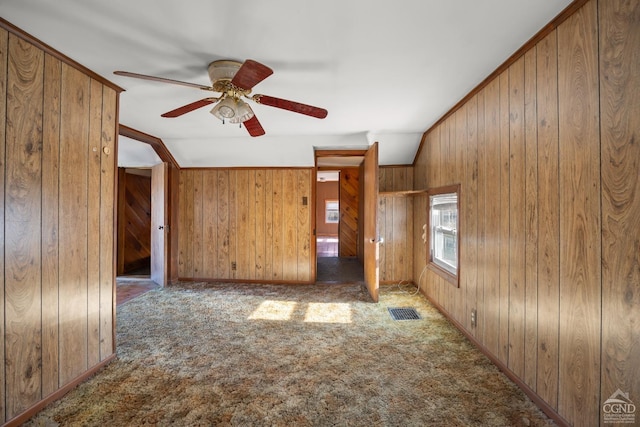 empty room with visible vents, wood walls, carpet flooring, and a ceiling fan