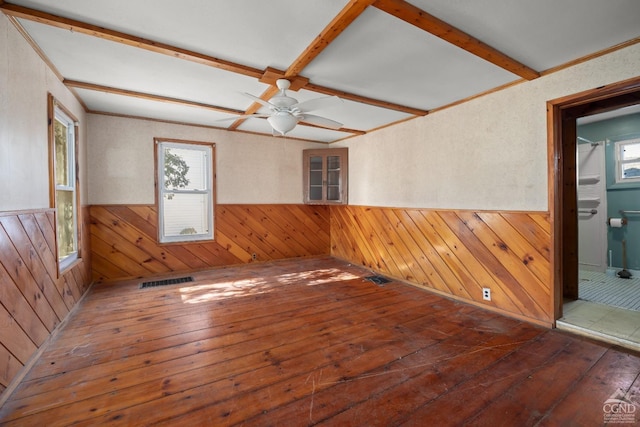 empty room featuring hardwood / wood-style floors, wainscoting, beam ceiling, and wooden walls