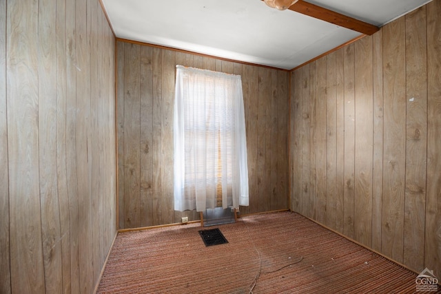 spare room with visible vents, wood walls, and beamed ceiling