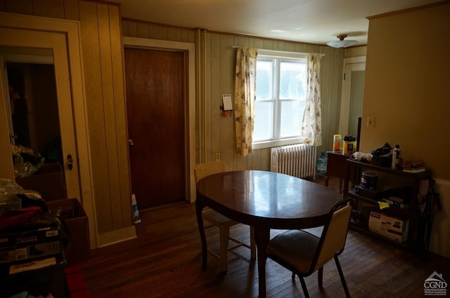 dining room featuring dark hardwood / wood-style flooring, wooden walls, and radiator heating unit