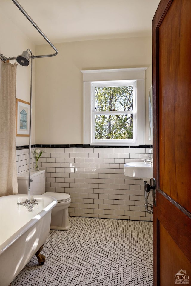 496 Clinton St, Hudson, NY 12534 - bathroom featuring a freestanding tub, tile walls, a wainscoted wall, tile patterned floors, and toilet