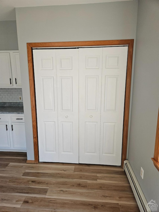 interior details with a baseboard radiator, backsplash, and wood finished floors