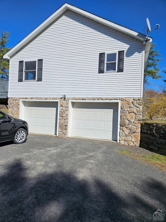 view of home's exterior with stone siding, an attached garage, and aphalt driveway