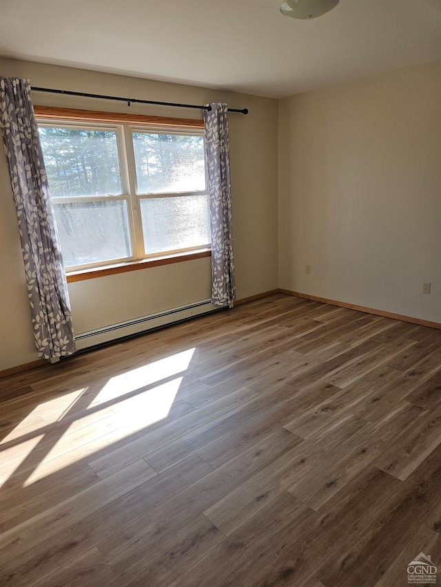 empty room with a baseboard radiator, a wealth of natural light, wood finished floors, and baseboards