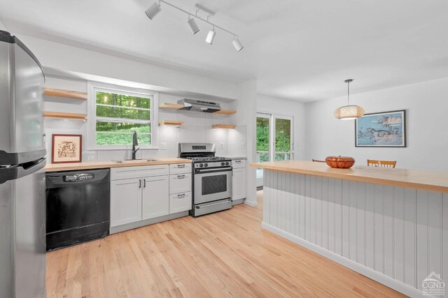 kitchen with butcher block counters, sink, stainless steel appliances, pendant lighting, and white cabinets